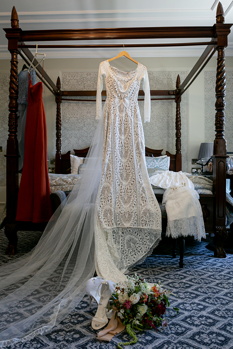 The brides wedding dress is seen hanging on a four post bed with the wedding bouquet and shoes before it, shot at the beautiful Ballyseede castle hotel, Tralee.