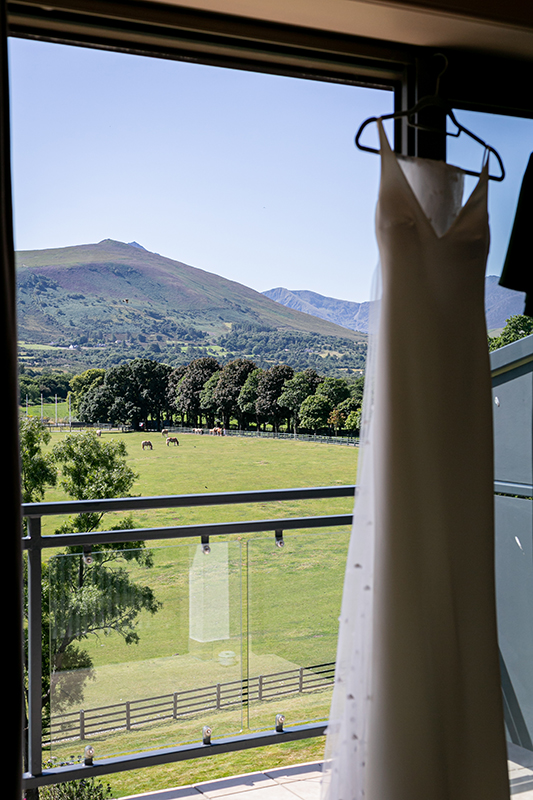 portrait photo of wedding dress hanging by window overlooking a mountain view