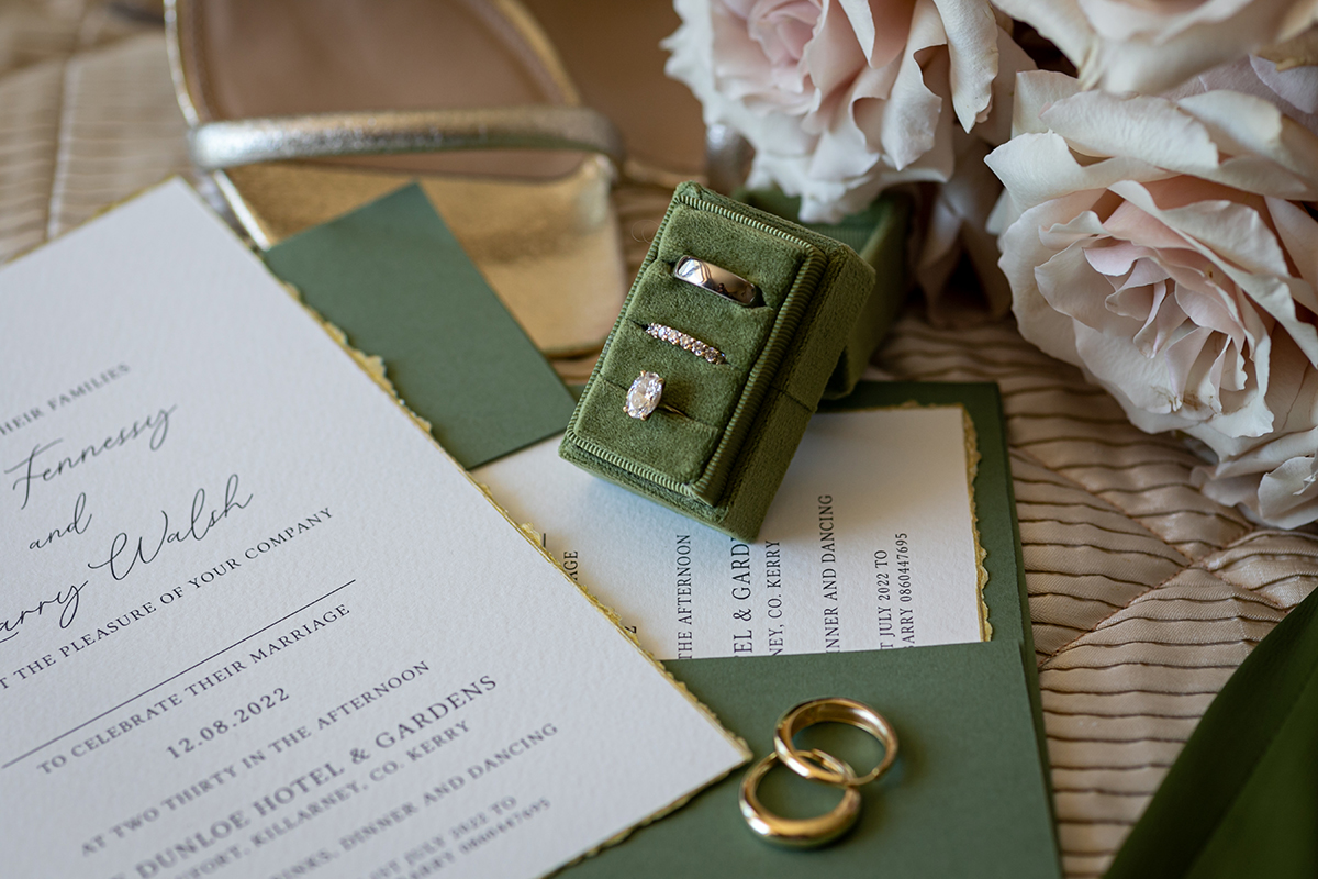 bride and grooms wedding rings in a green ring box placed next to wedding invitation