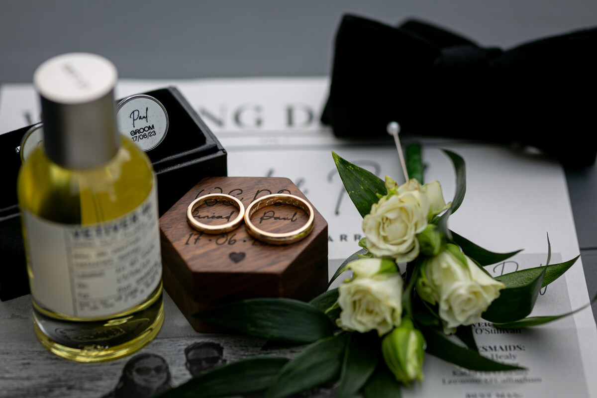 Styled shot of the wedding bands laying on top of the wooden ring box surrounded by aftershave, bowtie and florals.