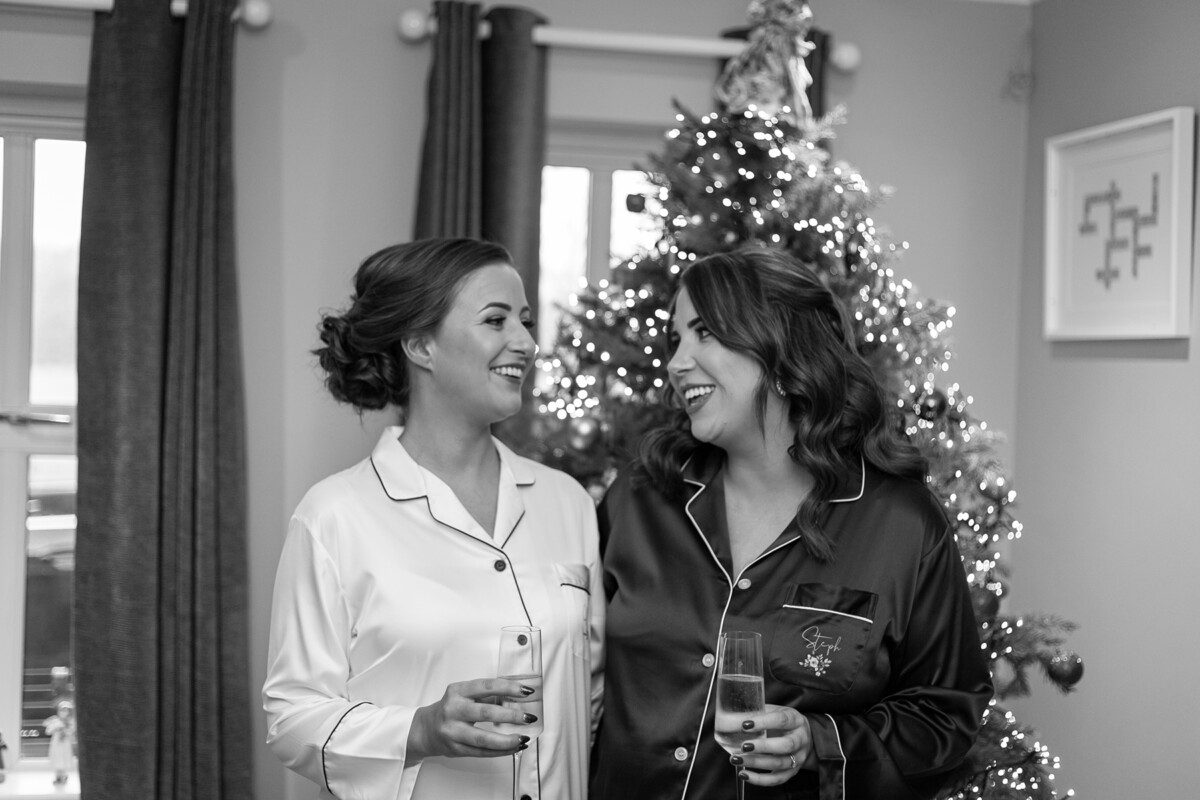 Black and white photograph of the bride and maid of honour wearing silk pyjamas in front of a Christmas tree in the beautiful Heights Hotel, Killarney.