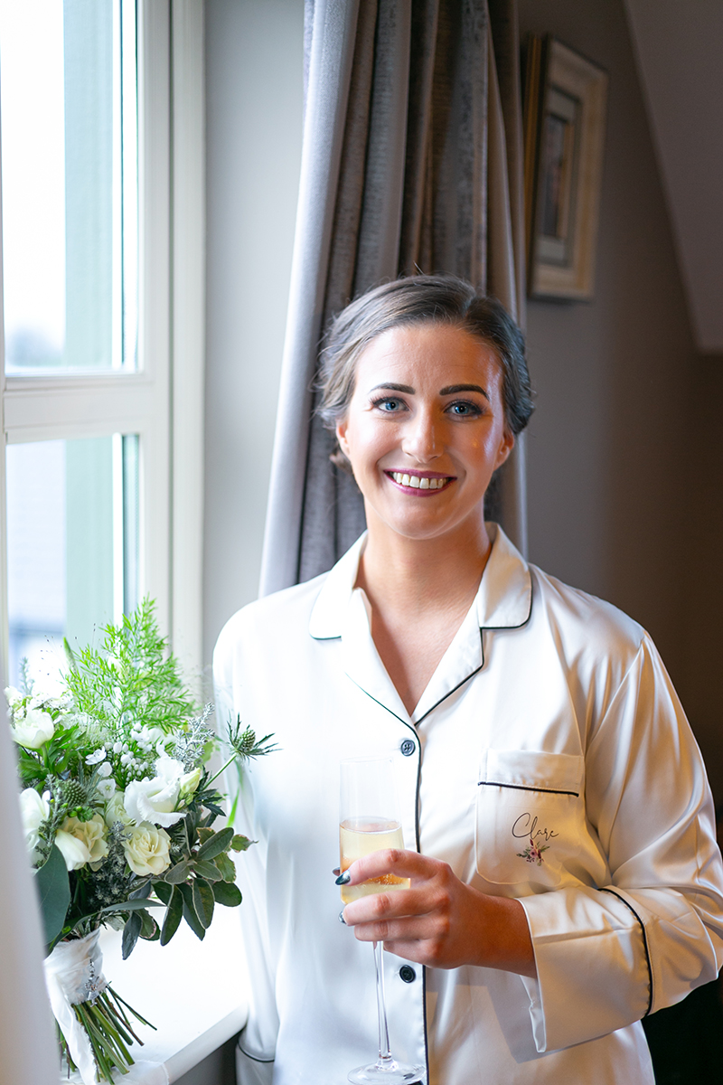 Portrait of the happy bride by a window of the Heights Hotel, holding a glass of champagne.