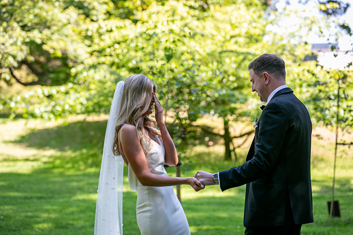 groom holding the brides hand during first look with green foliage in background