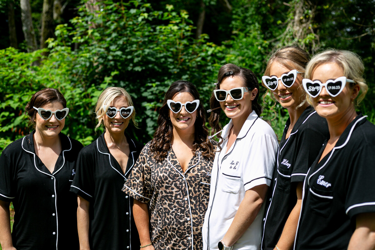 The bride and her bridesmaids in their pyjamas outside in the sunshine wearing heart shaped sunglasses on the grounds of Drumquinna Manor.
