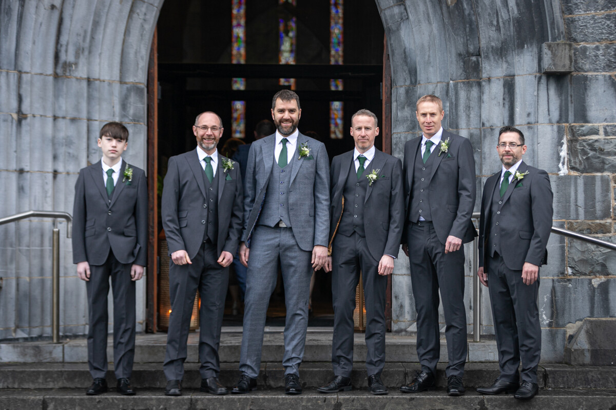 Groom and groomsmen stood in a line on the steps of St Marys cathedral, Killarney.