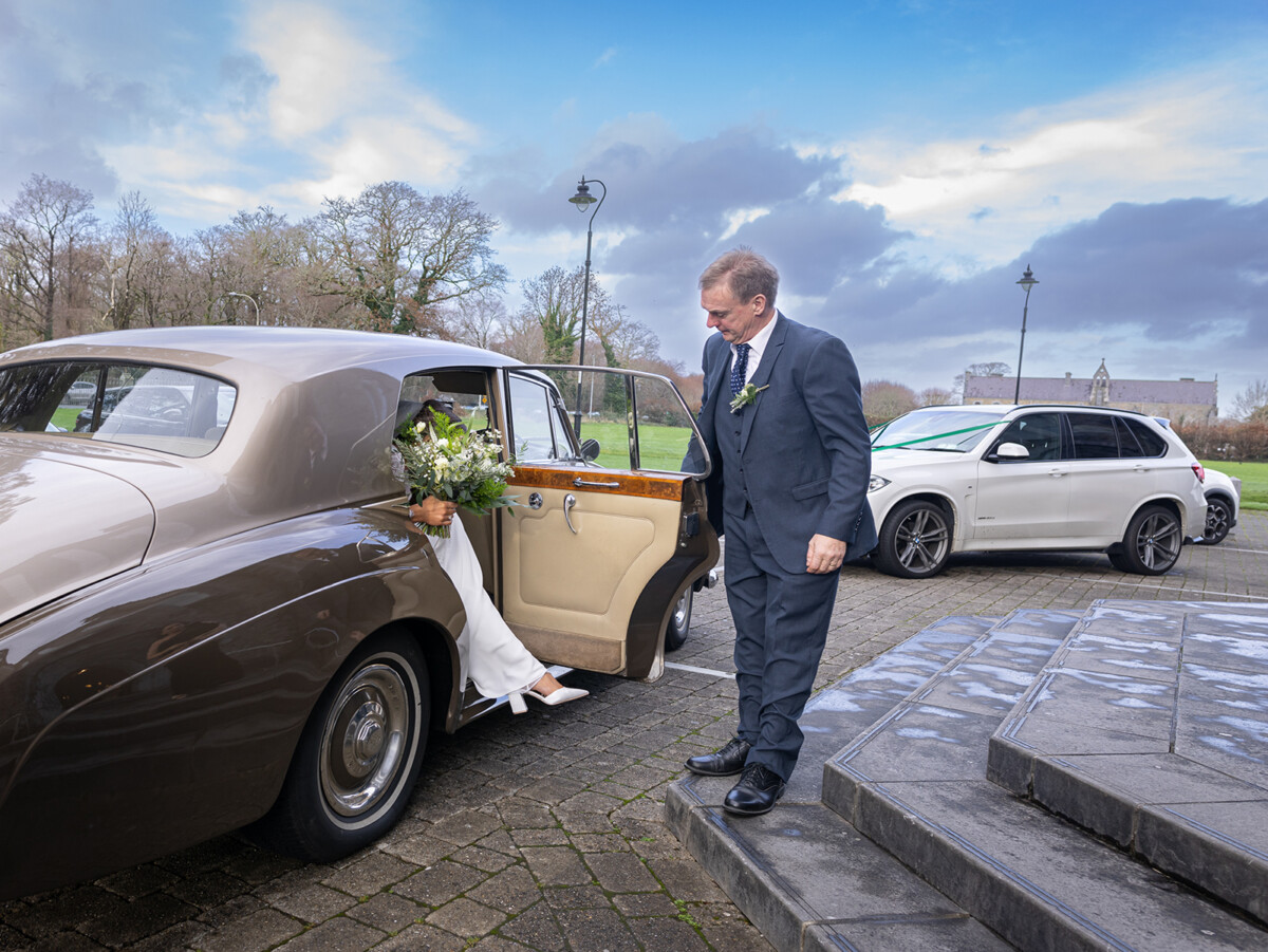 Father of the bride holds open the wedding car door for her outside of St Marys, Killarney.
