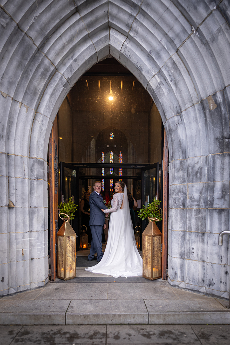 Bride and her father pose for a picture in the entrance arch of St Marys in Killarney.