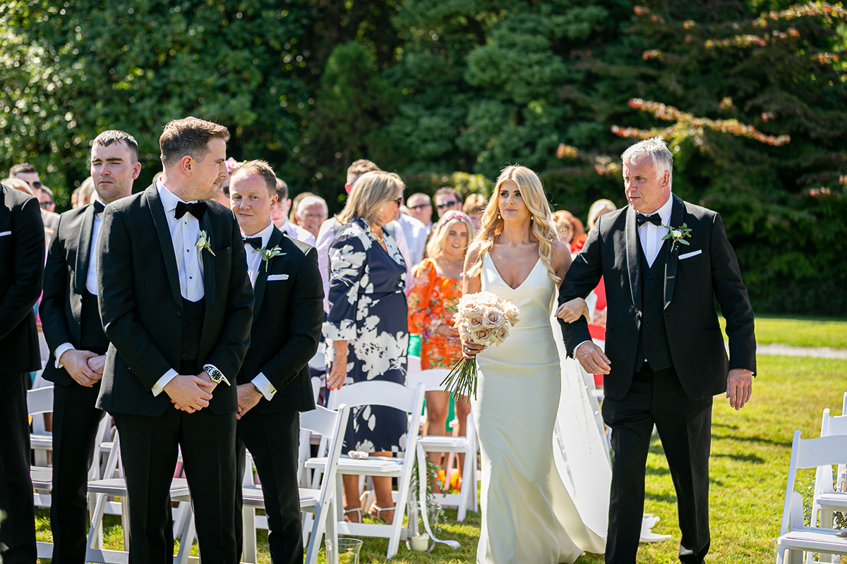 bride meets groom at the end of the aisle of their wedding set in the gardens of the dunloe hotel with wooded areas in the background