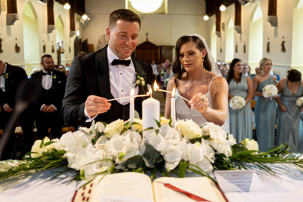 Bride and groom lighting a candle surrounded by white florals at the alter in Kenmare.