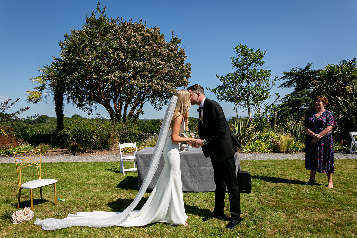 bride and groom share a kiss in the sunshine with the scenery of the dunloe hotel gardens in the background
