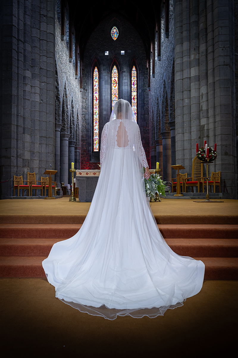 Portrait of the back of the brides dress standing at the alter of St Marys, Killarney.