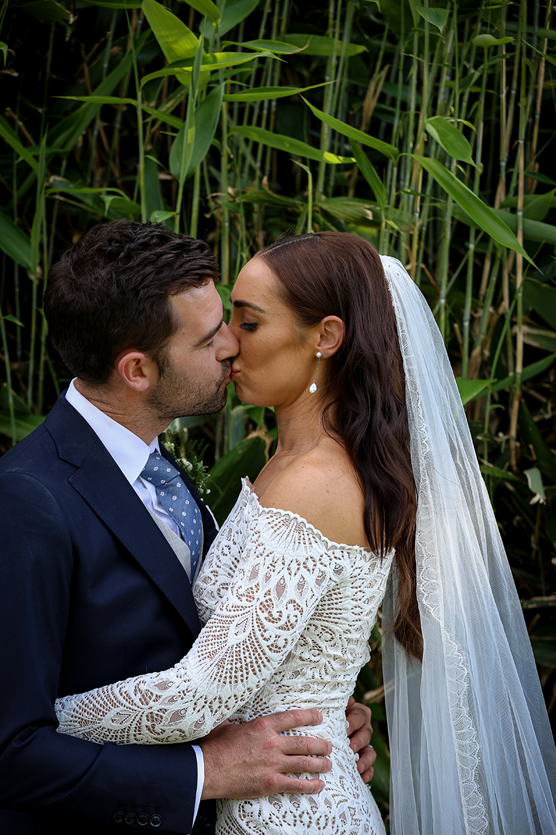The bride and groom share a kiss against a backdrop of green bamboo on the grounds of Ballyseede castle, Tralee.