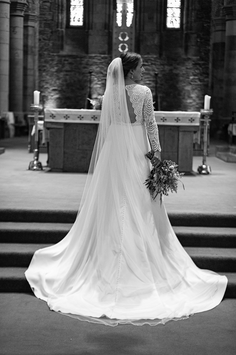 Black and white portrait of the back of the brides dress standing at the alter of St Marys, Killarney.