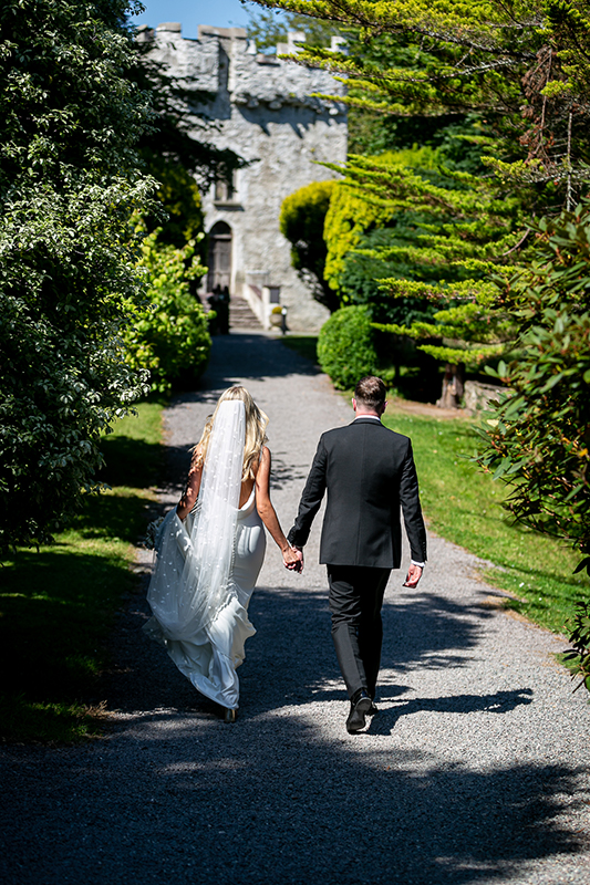 bride and groom walk hand in hand towards the castle with trees lining both sides of the path near the dunloe hotel