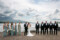 Bride and groom are pictured with their wedding party stood on either side of them, with the beautiful Kenmare bay and blue skies in the background.