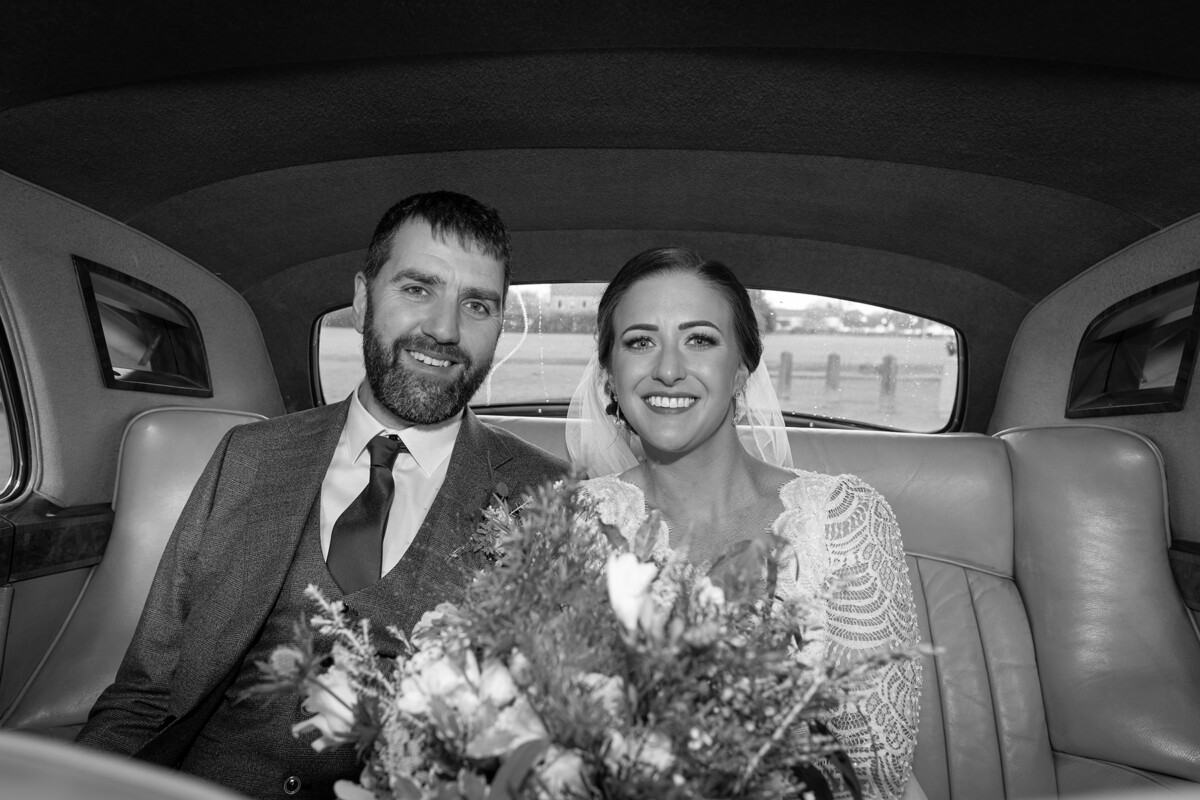 Black and white photograph of the newlyweds sitting in the back of their wedding car outside St Marys.