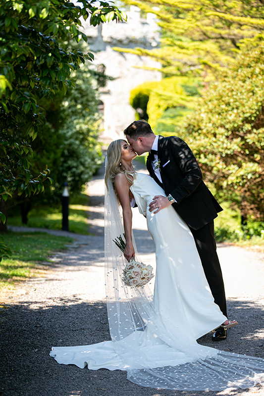 bride and groom share a kiss with a castle set in sunshine in the background near the dunloe hotel killarney