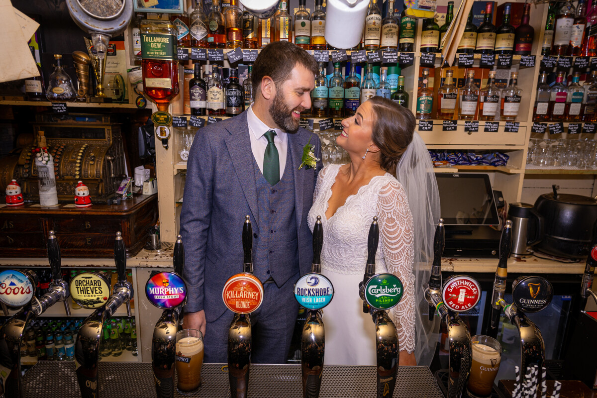 Bride and groom stand behind the bar at JM Reidys in Killarney.
