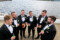Groom and his groomsmen stand in a circle smiling and enjoying a drink with soft waves of Kenmare bay in the background.