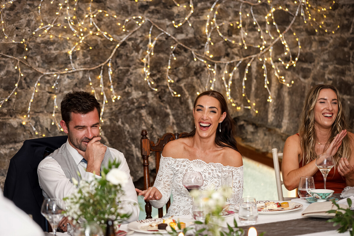 The bride and groom sit alongside another and laugh during the wedding speeches at the reception venue Ballyseede castle, Tralee.