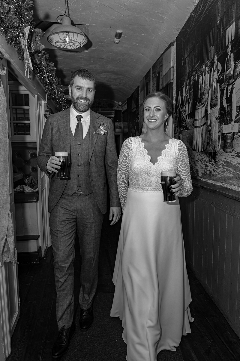 Black and white portrait of bride and groom carrying a pint of Guiness each at JM Reidys, Killarrney.