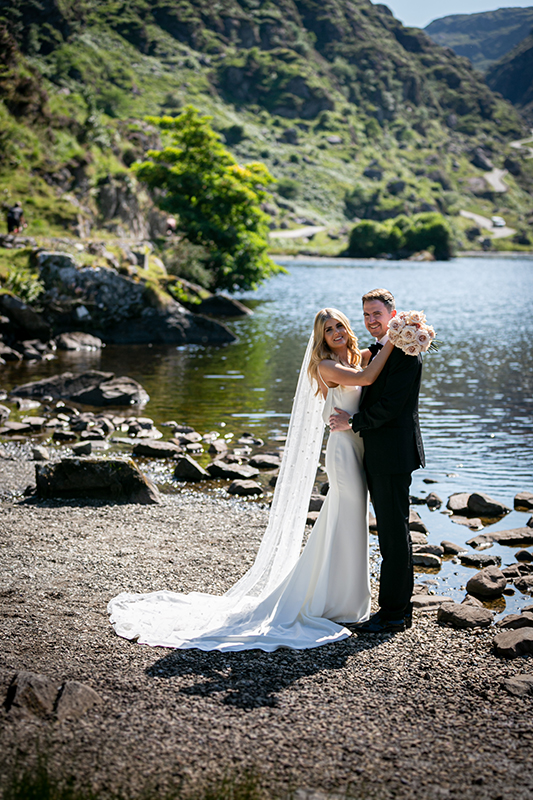 portrait of bride and groom on a sunny day stood by the water at the gap of dunloe killarney