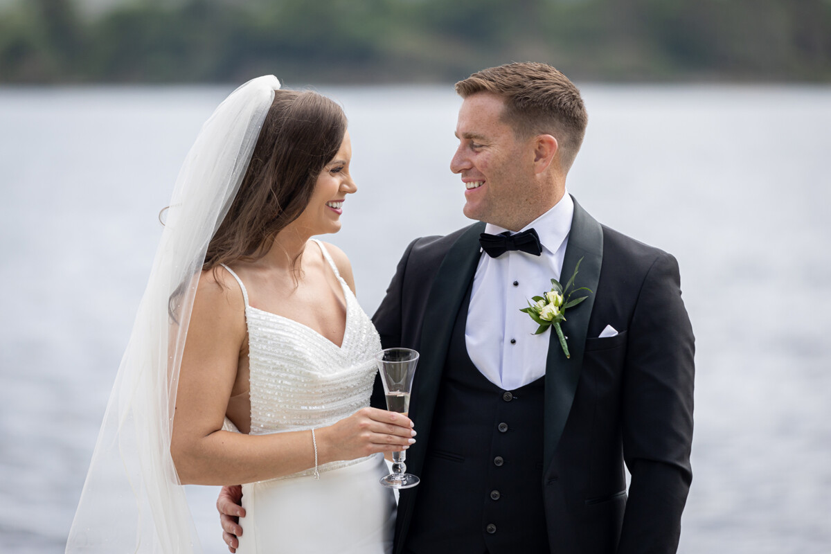 Bride and groom smiling at one another pictured at Kenmare bay with a blurred background.