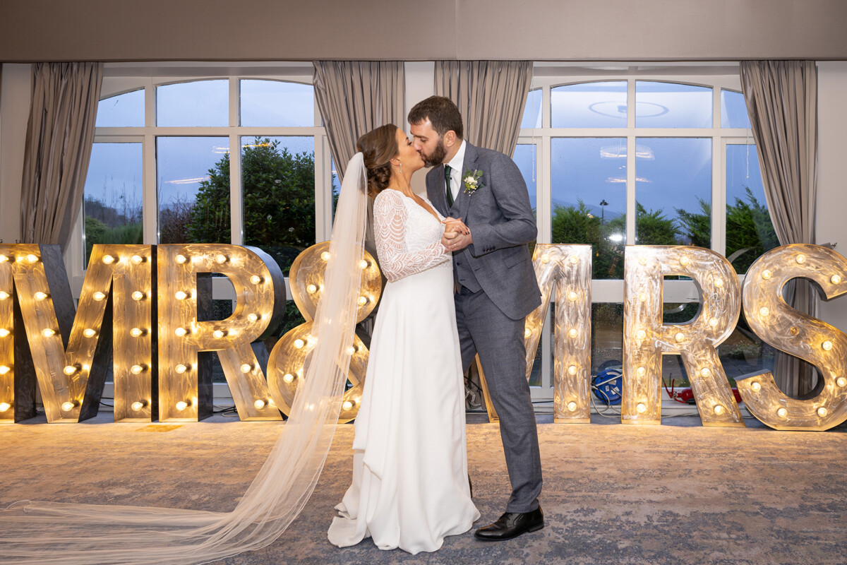 Bride and groom share a kiss in front of mr and mrs sign at their wedding reception in the Heights Hotel, Killarney.