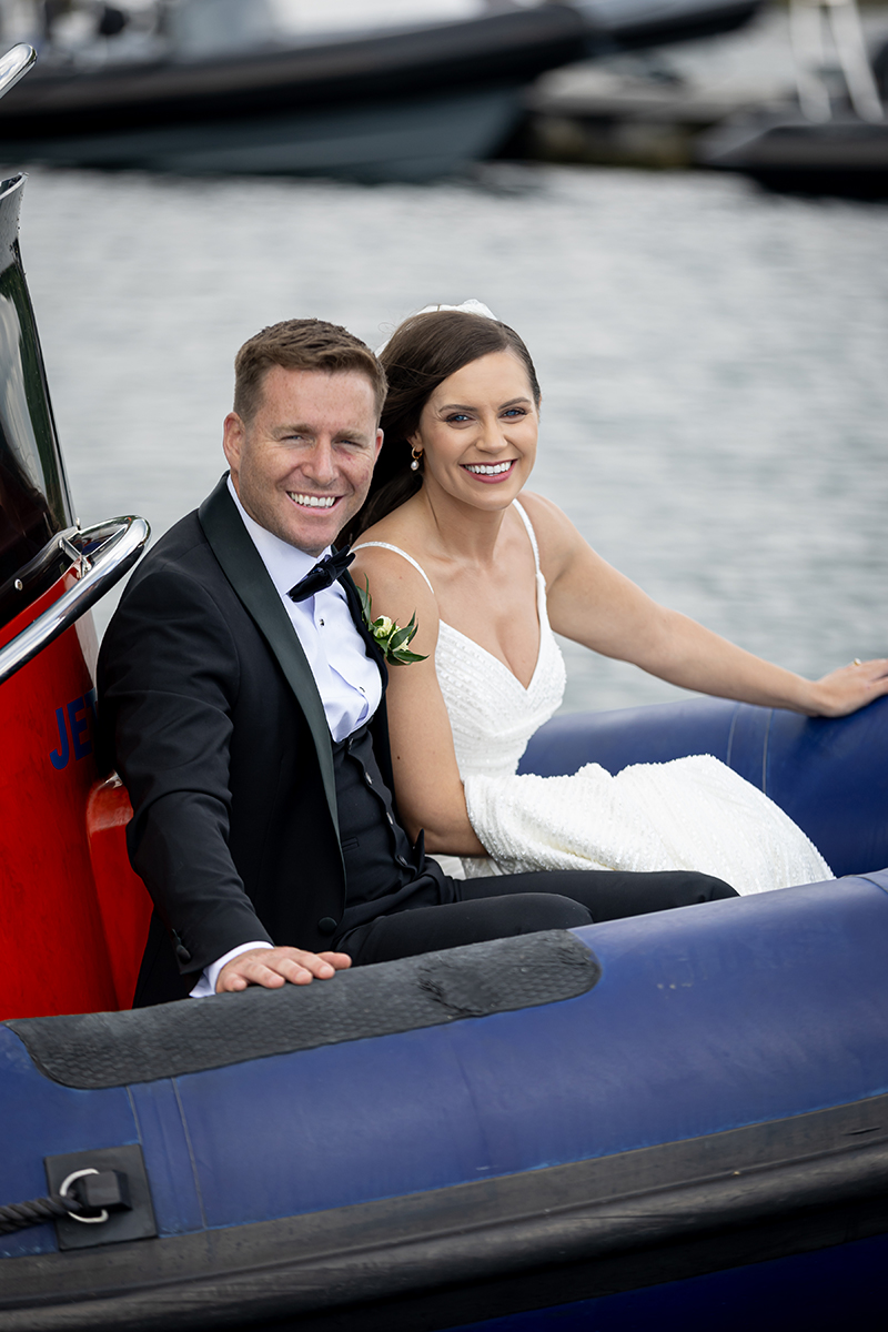 Close up of the bride and groom smiling at the camera, sat at the front of a boat touring the picturesque Kenmare bay.