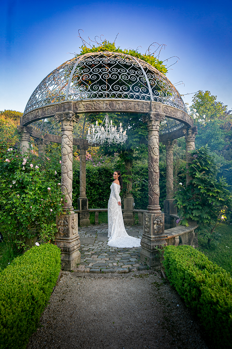 The bride stands in the centre of the round stone gazebo surrounded by foliage at Ballyseede hotel, Tralee.