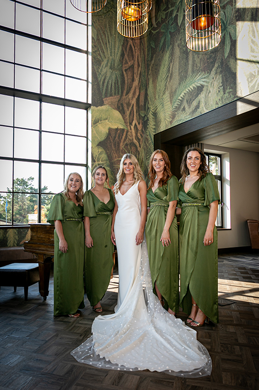 the bride and her bridesmaids wearing green stood by a window indoors of the dunloe killarney