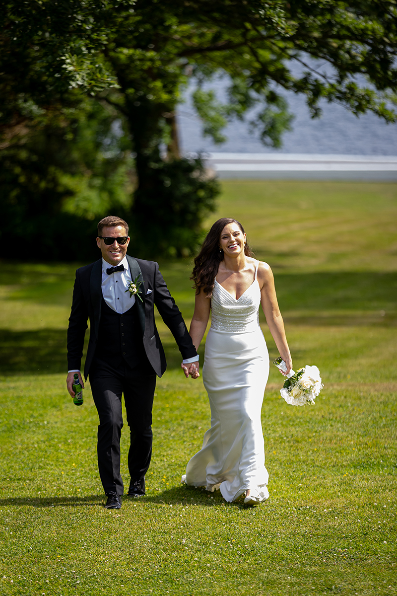 Bride and groom walk hand in hand with big smiles on their faces through the grounds of Dromquinna Manor.