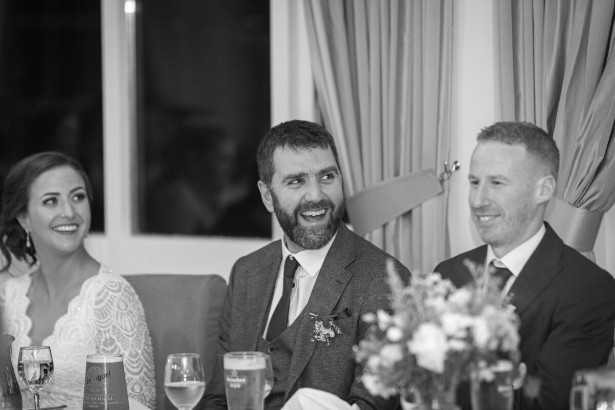 Black and white photograph of the groom and bride laughing during the wedding speeches in the Heights Hotel, Killarney.