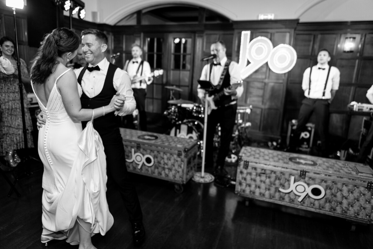 Bride and groom share their first dance with the wedding band pictured in background.