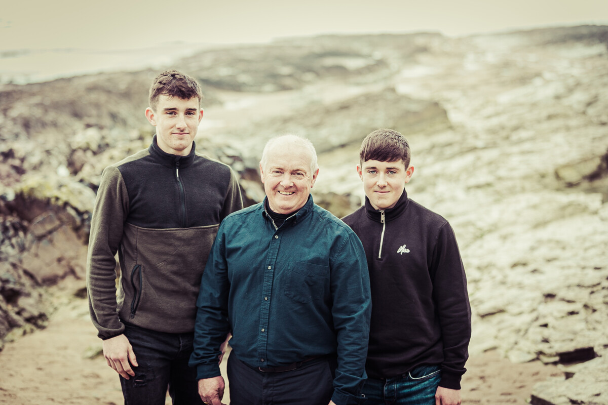 beach portrait of a father and his two sons at ballyheigue beach with rocky landscape in background and middle ground