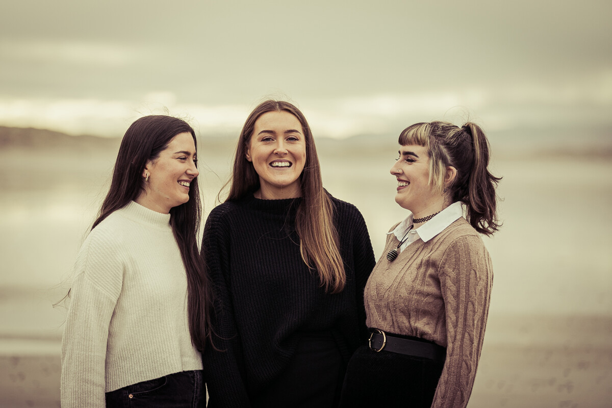 close up beach portrait of three sisters smiling with a soft blurred back ground of ballyheigue beach