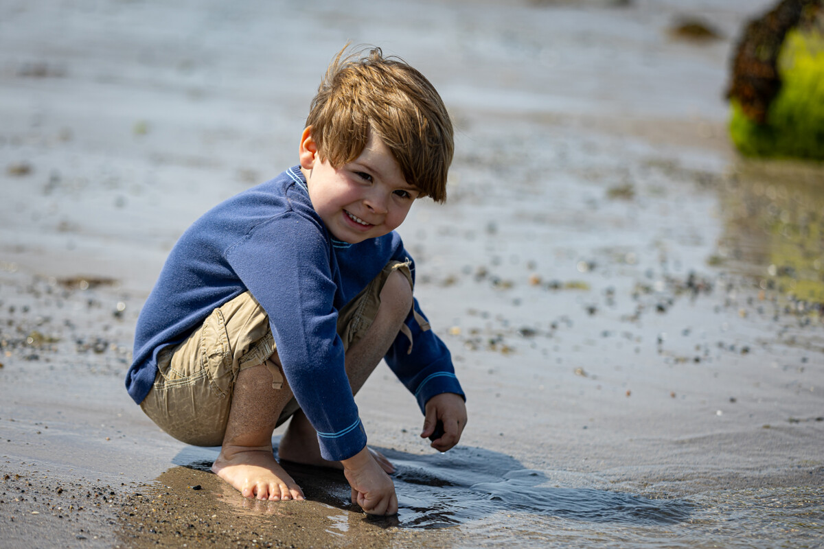 Beach portrait of a little boy crouching in the sand at a Castlegregory beach.