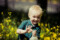 Portrait of a little boy smiling at the camera holding a teddy bear surrounded by flowers in a Dublin park.