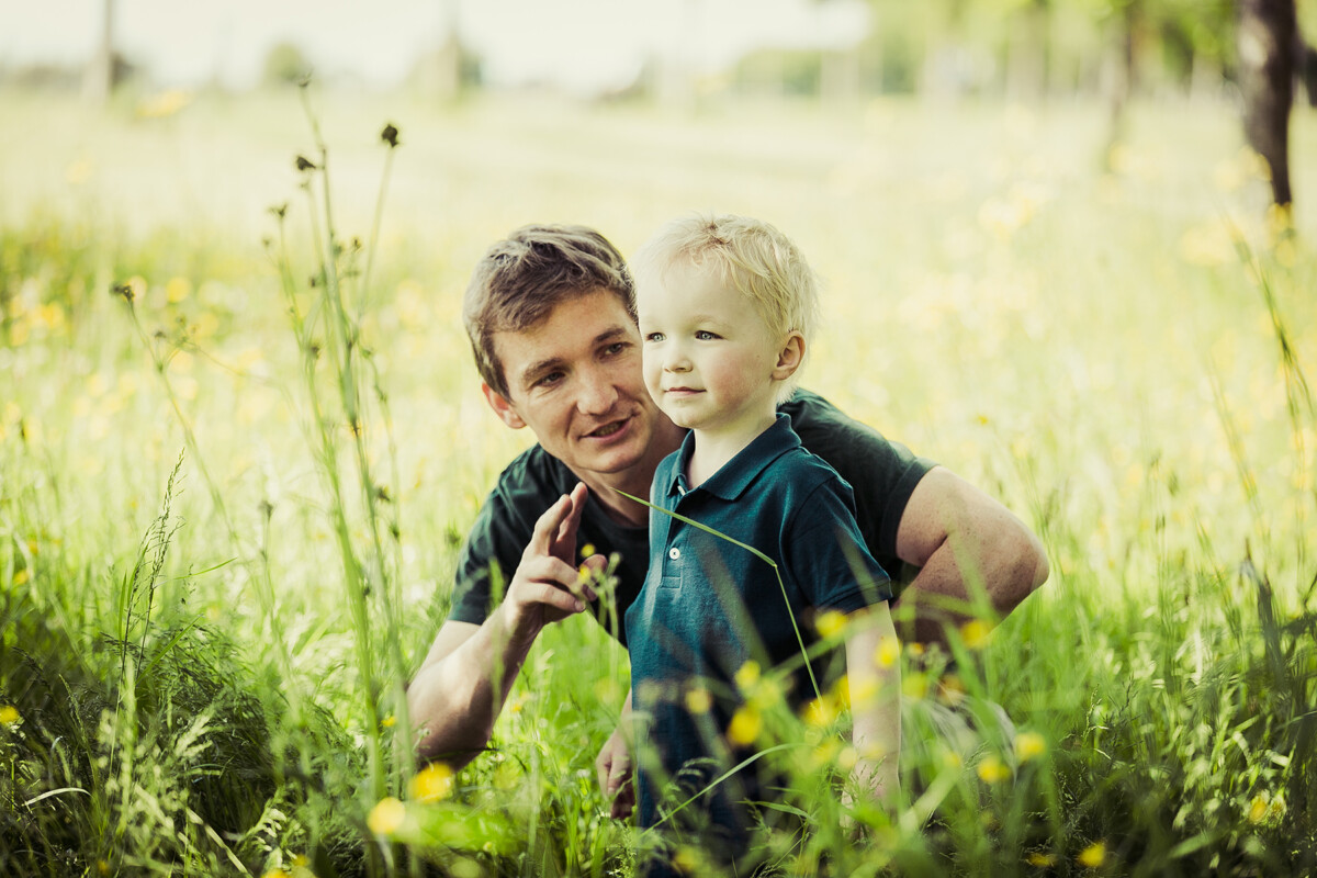 Family portrait of a father and son crouching amongst the grass in a Dublin park.