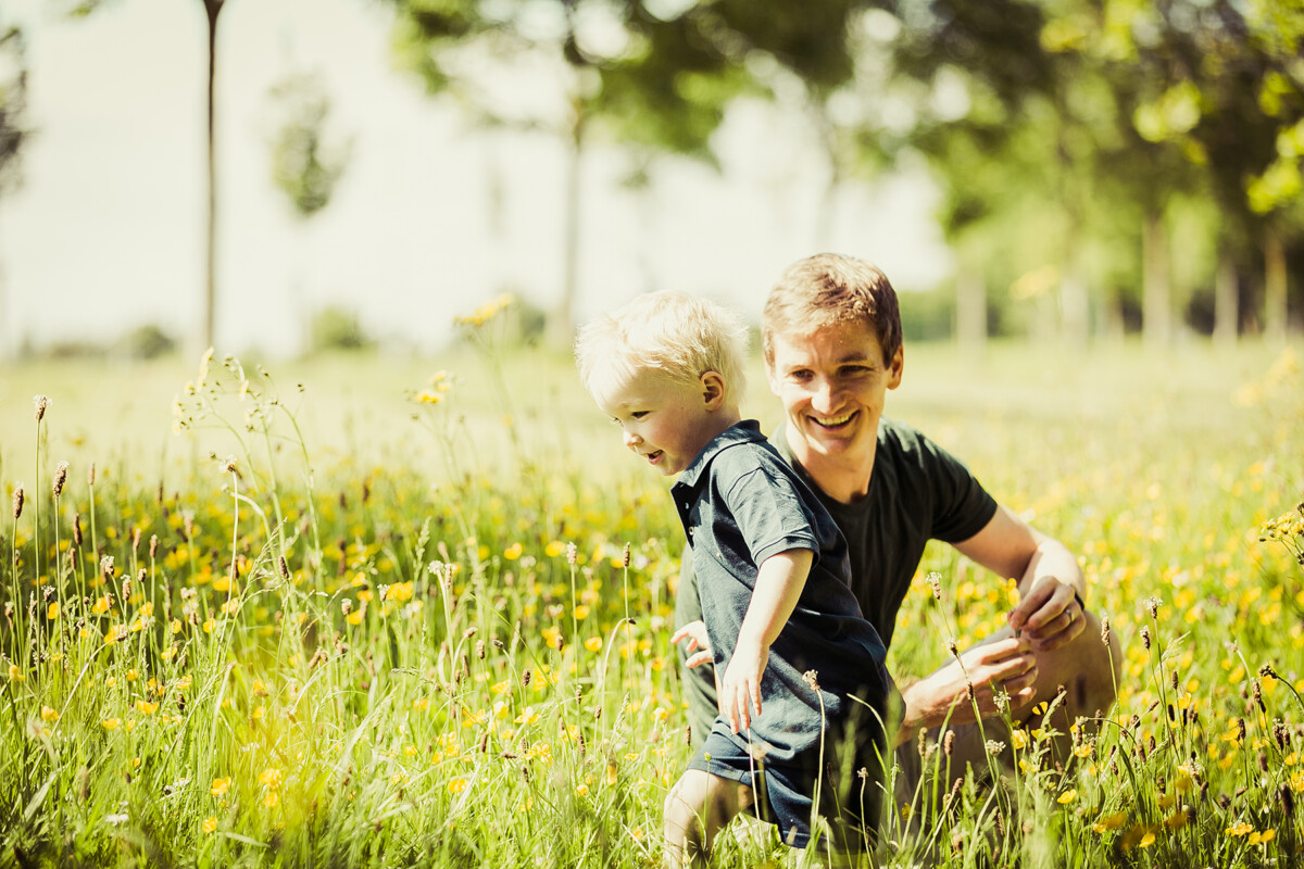 Family portrait of a father and son playing amongst the flowers and grass in a park.