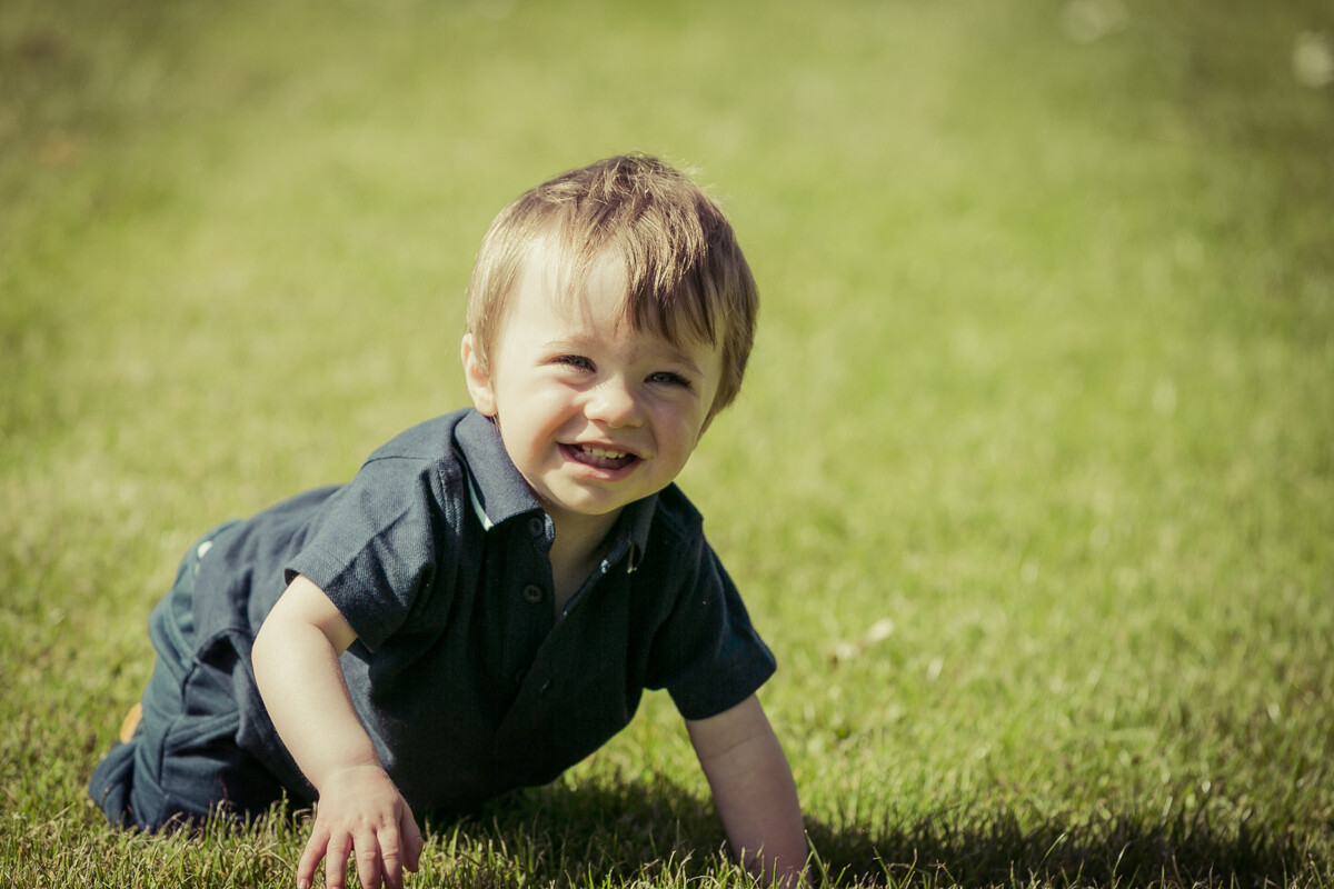 Portrait of a little boy smiling at the camera and crawling in the grass at a local Dublin park.