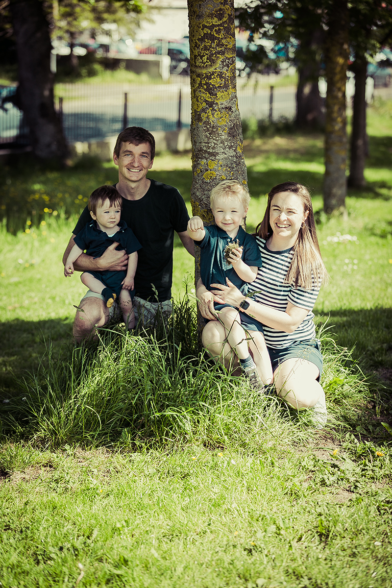 Family portrait of parents and their sons crouching in front of a tree at a local Dublin park.