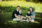 Family portrait of a couple and their sons smiling at the camera and sitting in the grass of a local Dublin park.