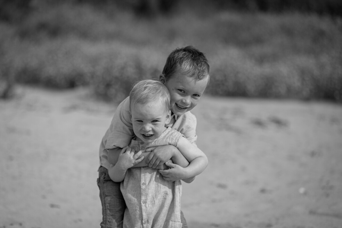 black and white portrait of a young boy hugging his little brother both facing the camera at fenit beach