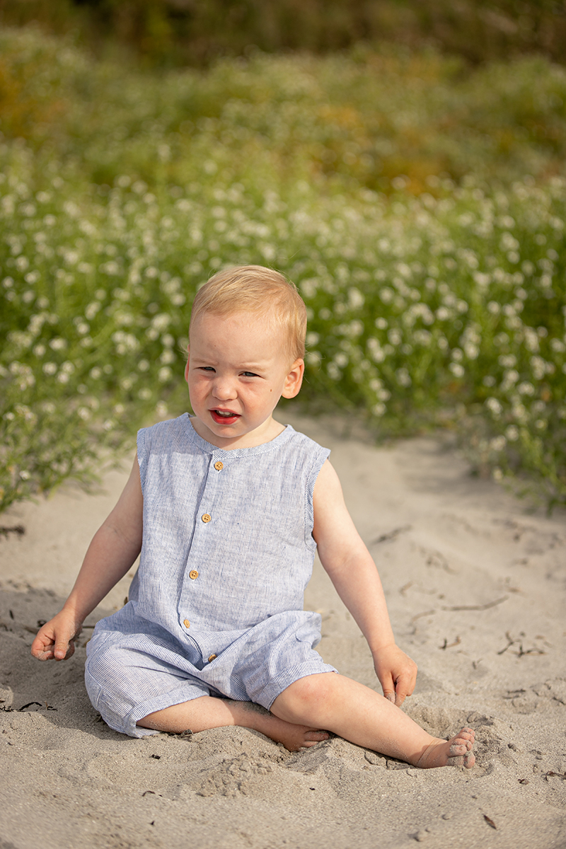 beach portrait of a little boy sitting in the sand at fenit beach with a backdrop of the beach dunes