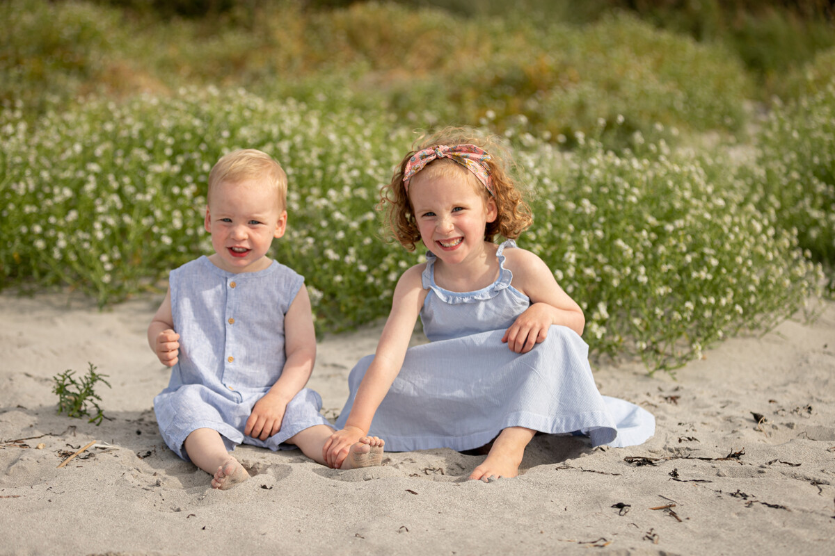 beach portrait of a girl and her little brother sitting in the sand at fenit beach with a backdrop of the beach dunes