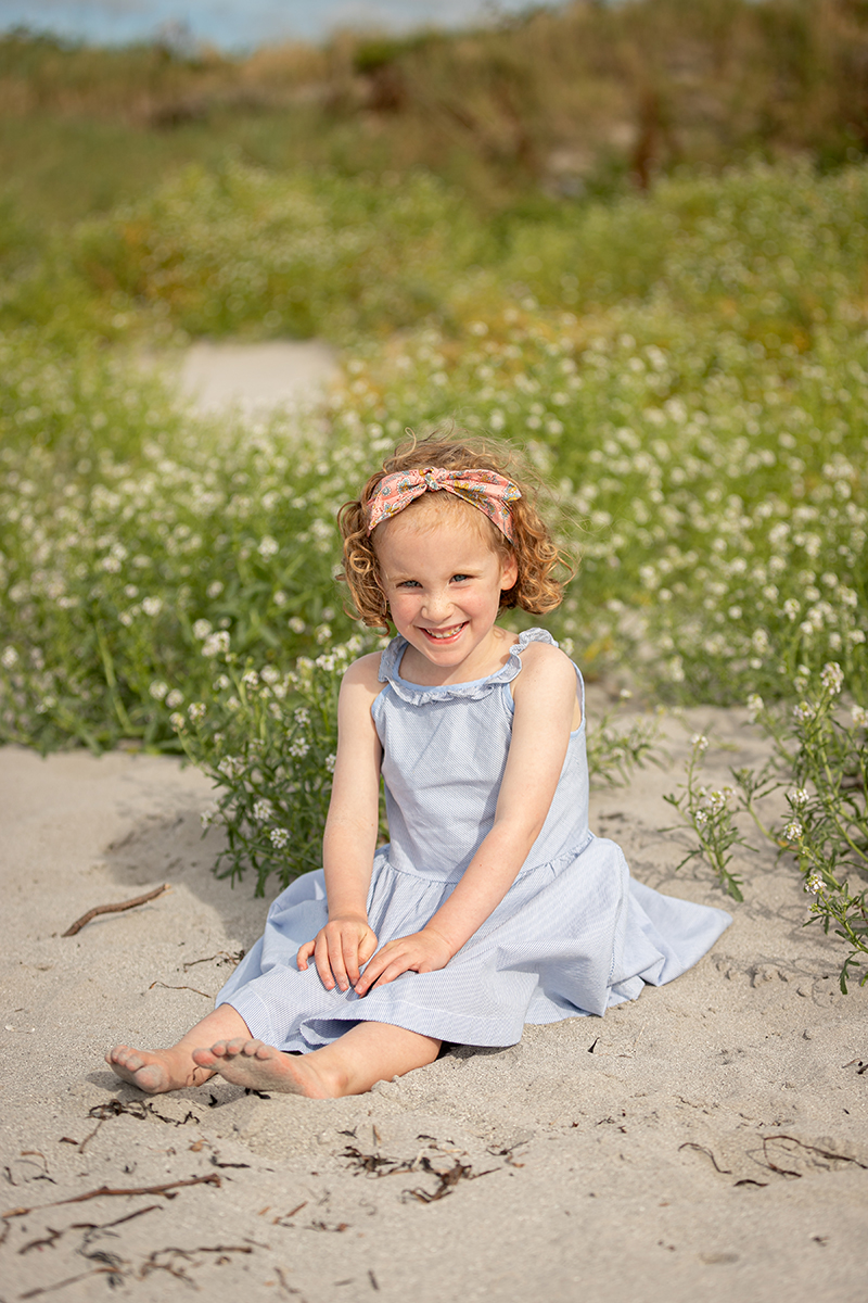 beach portrait of a little girl sitting in the sand at fenit beach with a backdrop of the beach dunes