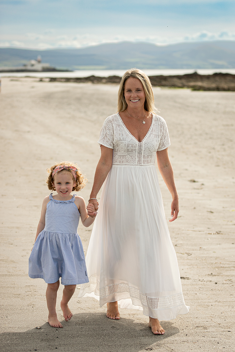beach portrait of mother and daughter facing the camera at fenit beach with mountains and blue sky in background