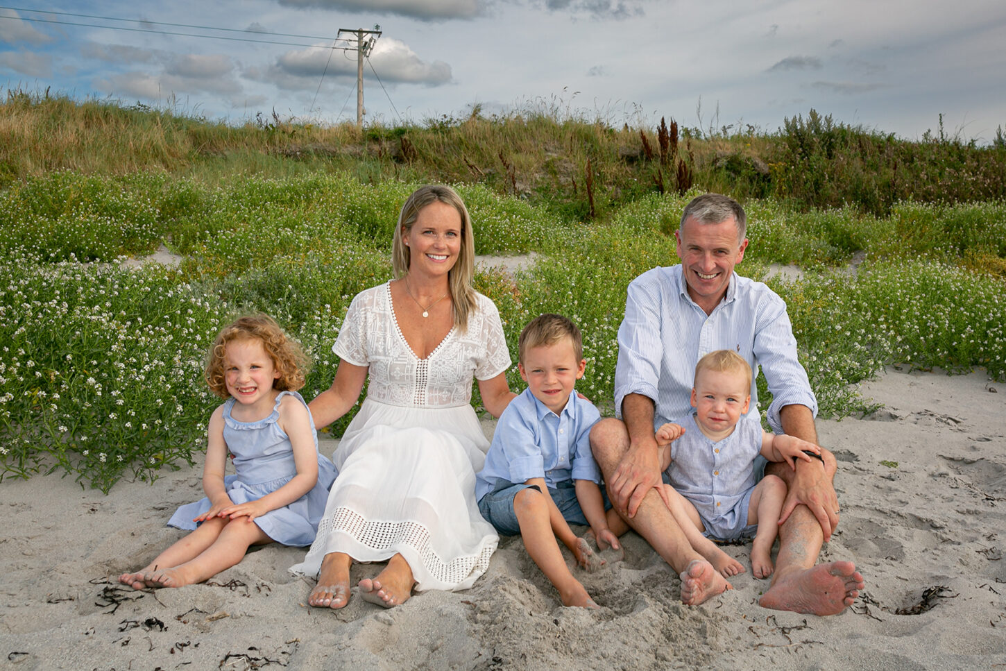 beach portrait of family of 5 sitting in the sand at fenit beach with dramatic sky