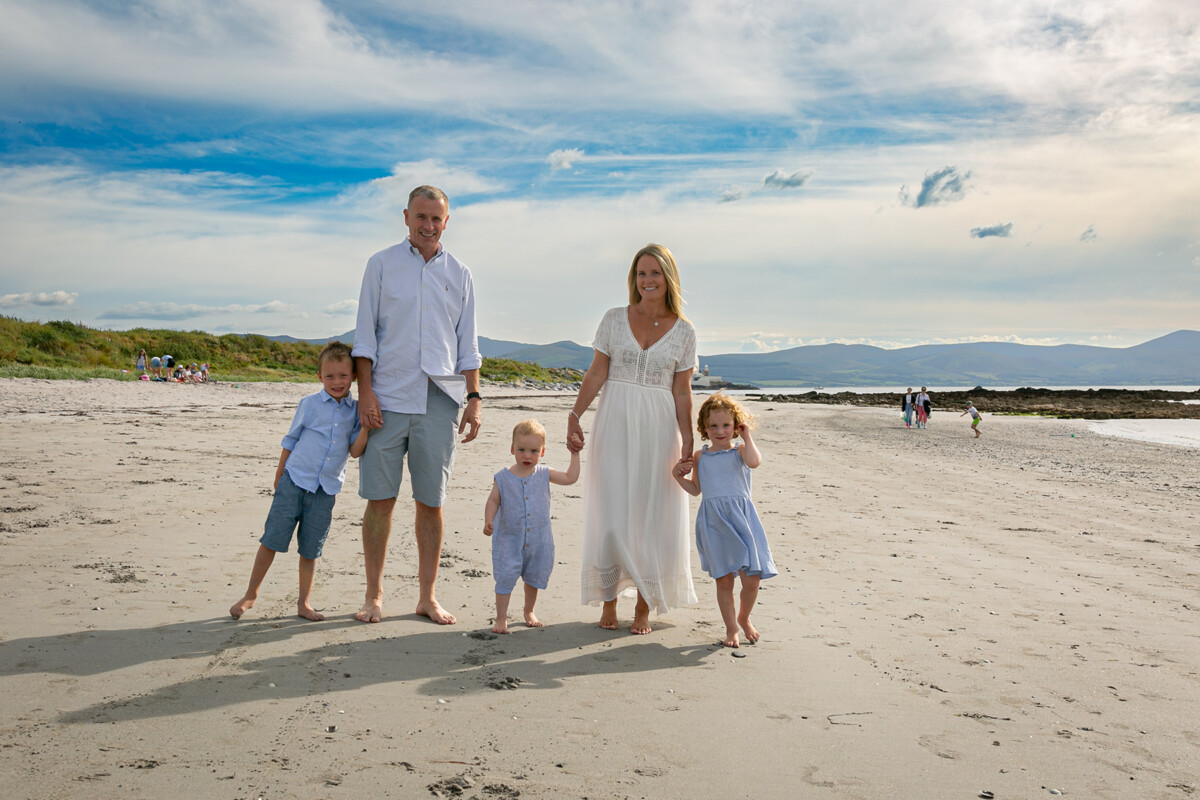 beach portrait of family of 5 standing on the sand at fenit beach with blue skies and mountains in the background